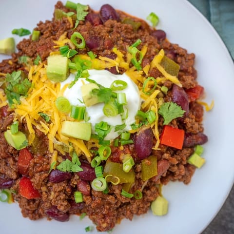 Thick, spicy Chili con Carne with a vibrant red hue, showcasing ground beef and vegetables simmering.