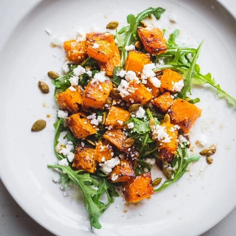 A vibrant bowl of roasted sweet potato salad featuring caramelized sweet potatoes, peppery greens, and creamy feta cheese.  