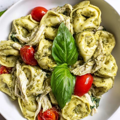Steam rises from a serving of Creamy Pesto Tortellini Skillet topped with fresh basil, cherry tomatoes, and spinach, ready for a quick weeknight dinner.