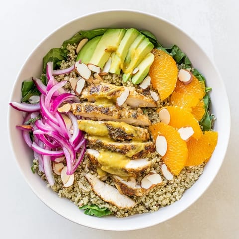Freshly grilled herb-marinated chicken rests atop a colorful salad bowl filled with quinoa, orange segments, and creamy avocado slices.  