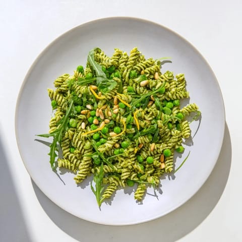 Fork-tender fusilli pasta salad with fresh basil pesto, sweet peas, and peppery arugula in a serving bowl.
