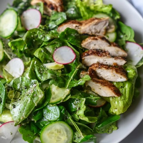 Sliced grilled chicken rests atop crisp mixed greens, cucumber, and radish in this Spring Detox Chicken Salad, drizzled with bright lemon vinaigrette.  
