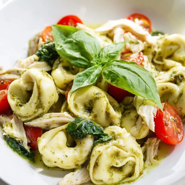 Rich, creamy pesto sauce clings to every tortellini and chicken piece in this skillet meal, garnished with Parmesan and vibrant greens for a comforting Italian-American dinner.