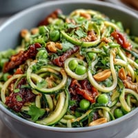 Healthy Easy Zucchini Noodle Stir-Fry with Peanut Sauce in a colorful skillet, garnished with chopped peanuts and cilantro, ready to serve.